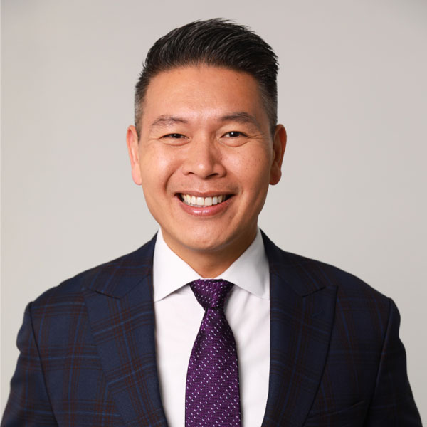 Headshot of Derek Tran in a patterned blue blazer with a purple and white polka dot tie.