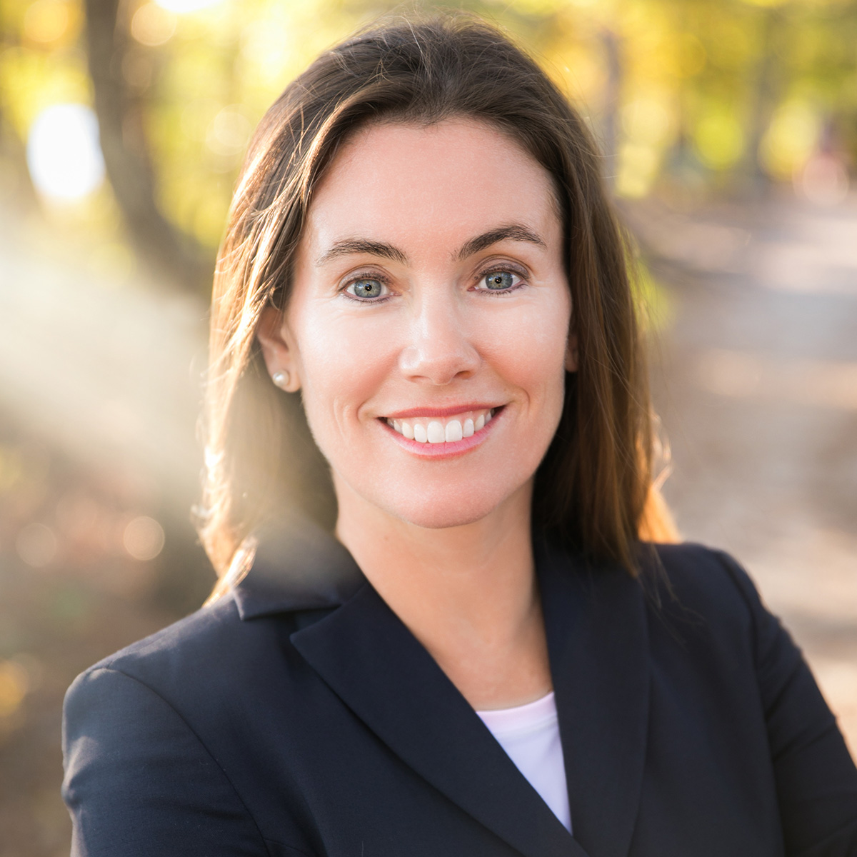 Headshot of Missy Cotter Smasal smiling in a black blazer with long straight hair and a glowy natural scenery.