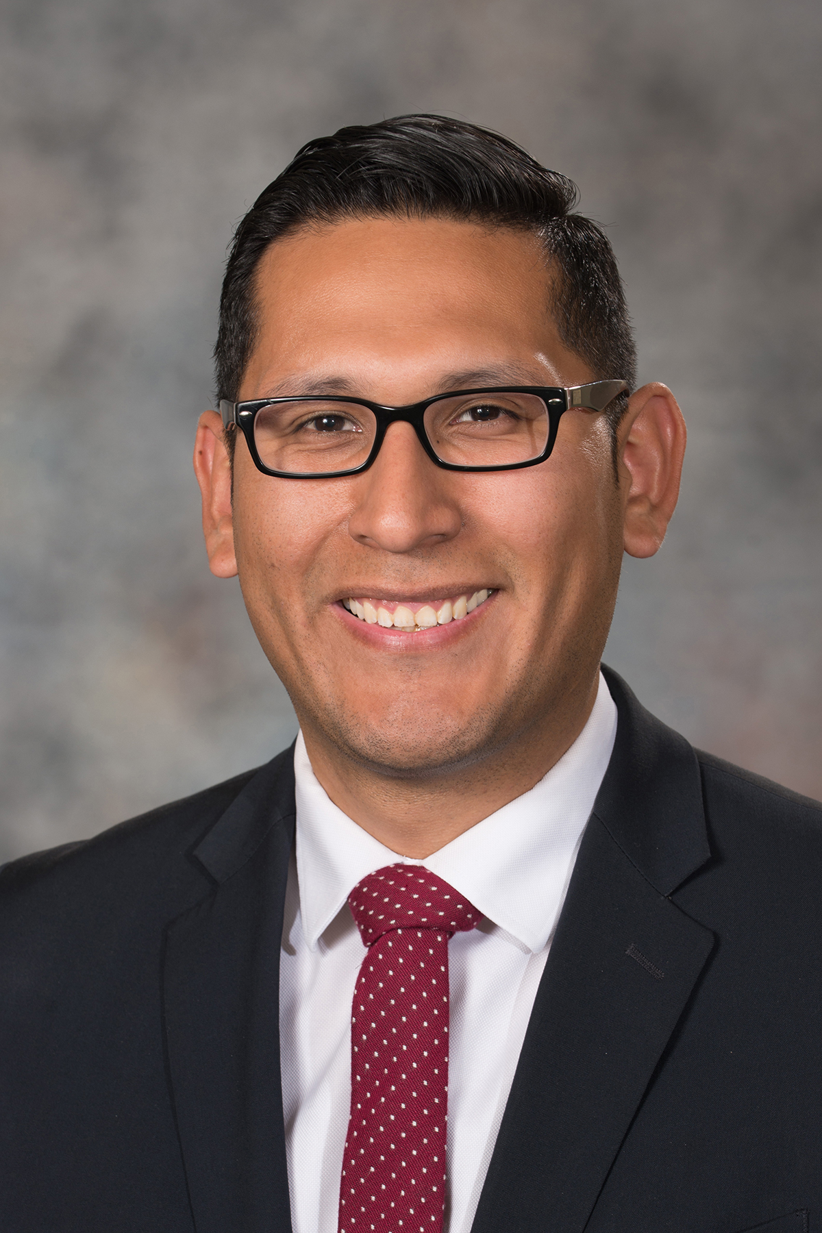 Headshot of Tony Vargas smiling in a black blazer and a white shirt with polka dot red and white tie.