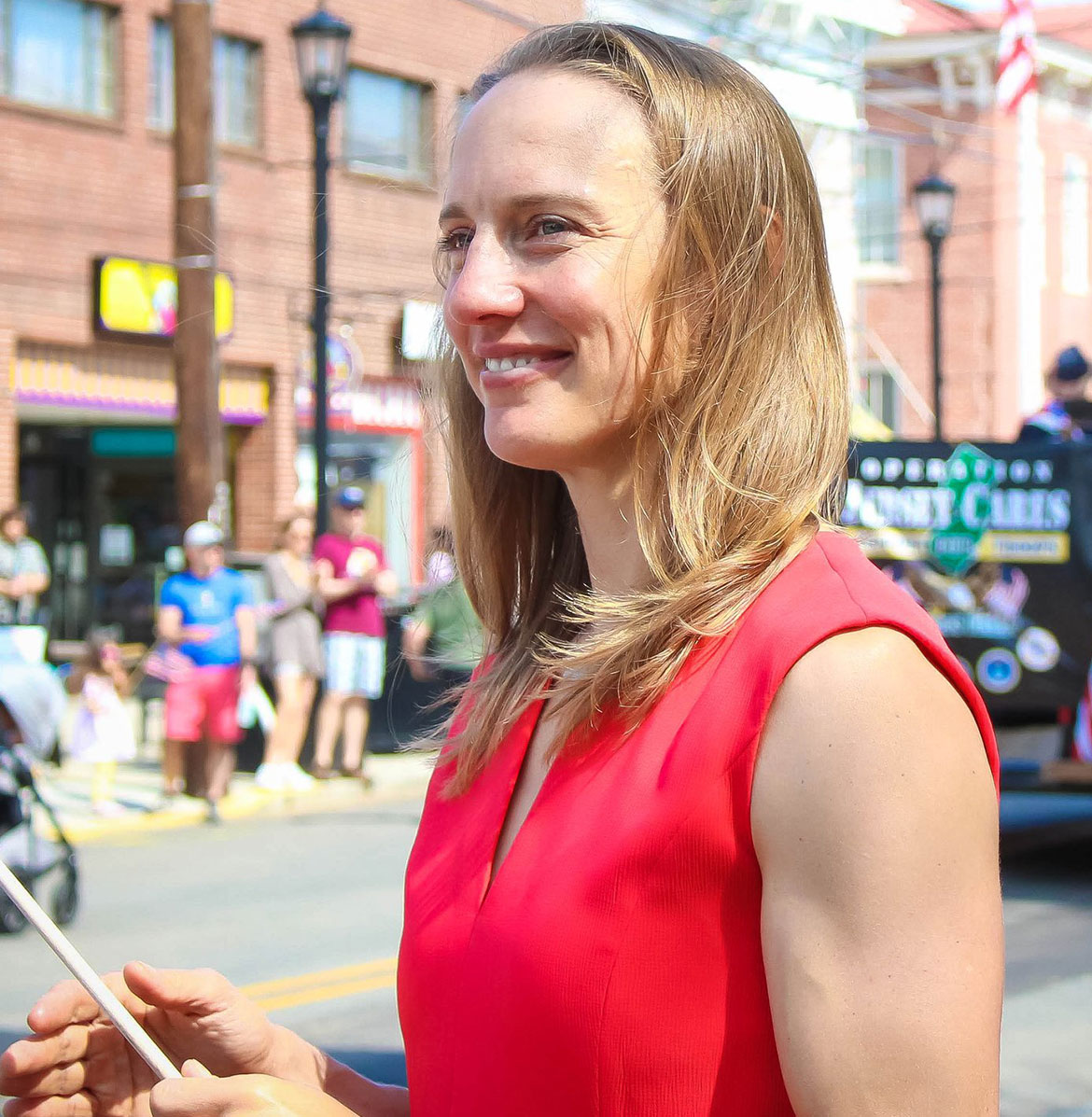 Susan Altman in a red top smiling off into the distance while holding something in her hand.