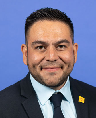 Headshot of Gabriel Vasquez smiling at the camera with a black suit jacket and tie with a blue shirt.