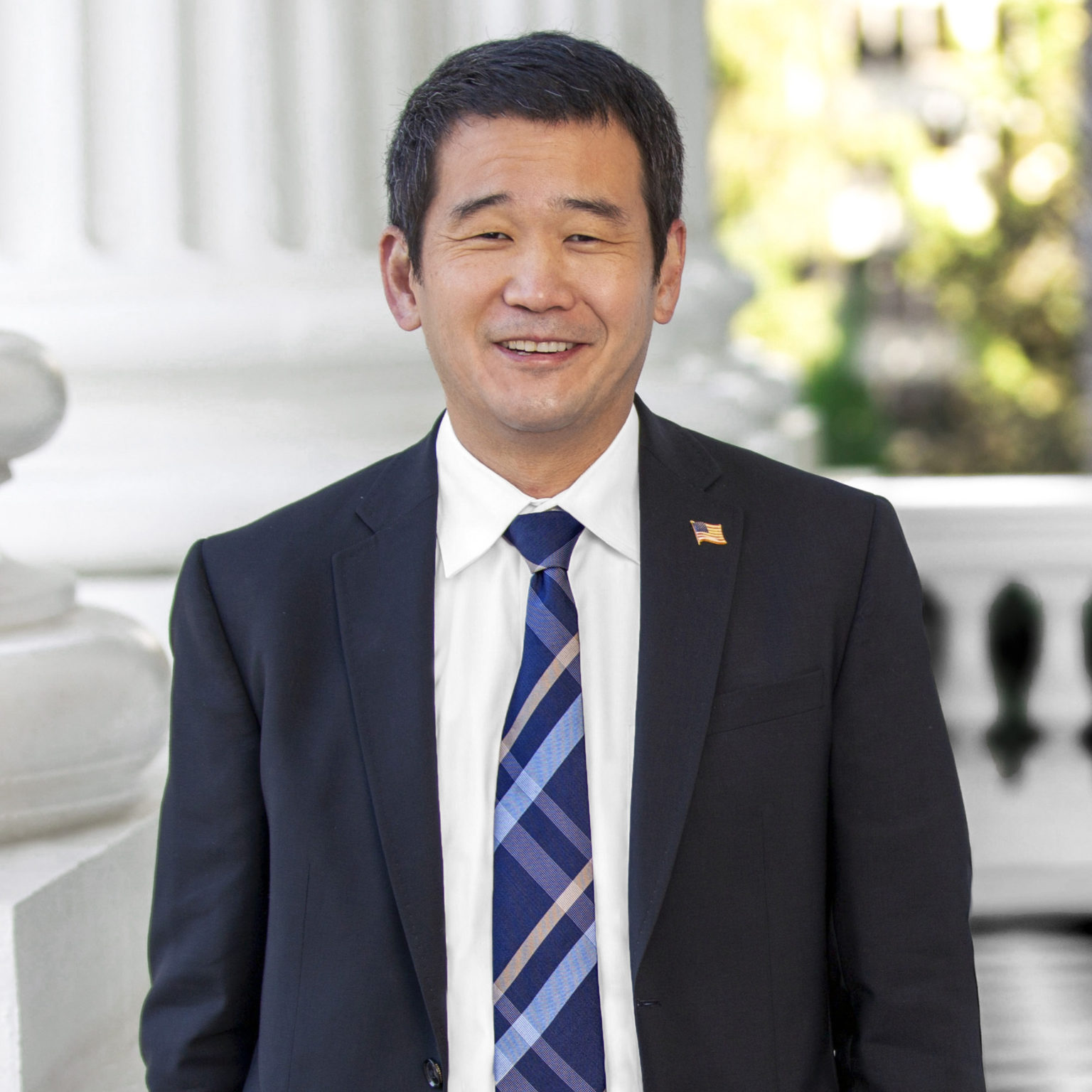 Headshot of Dave Min in a dark suit with a striped blue tie and white shirt.