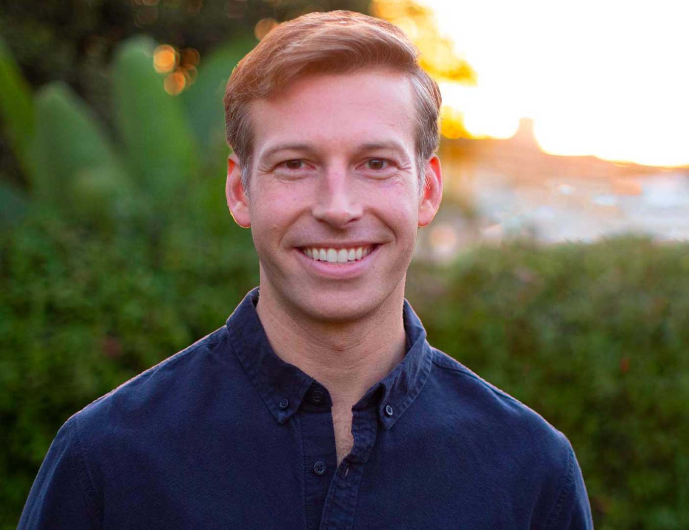 Headshot of Will Rollins with an organic nature background and a blue shirt.