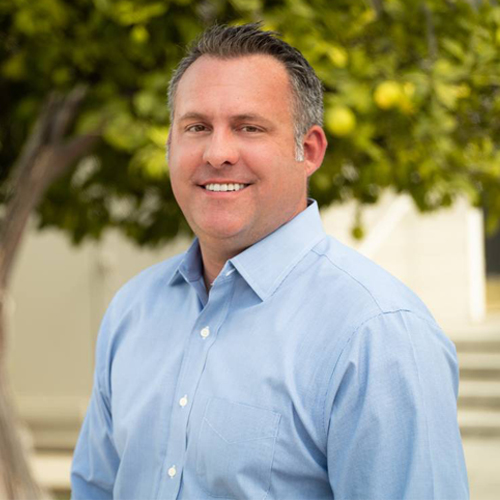 Headshot of Adam Gray in a blue shirt with a tree in the background.