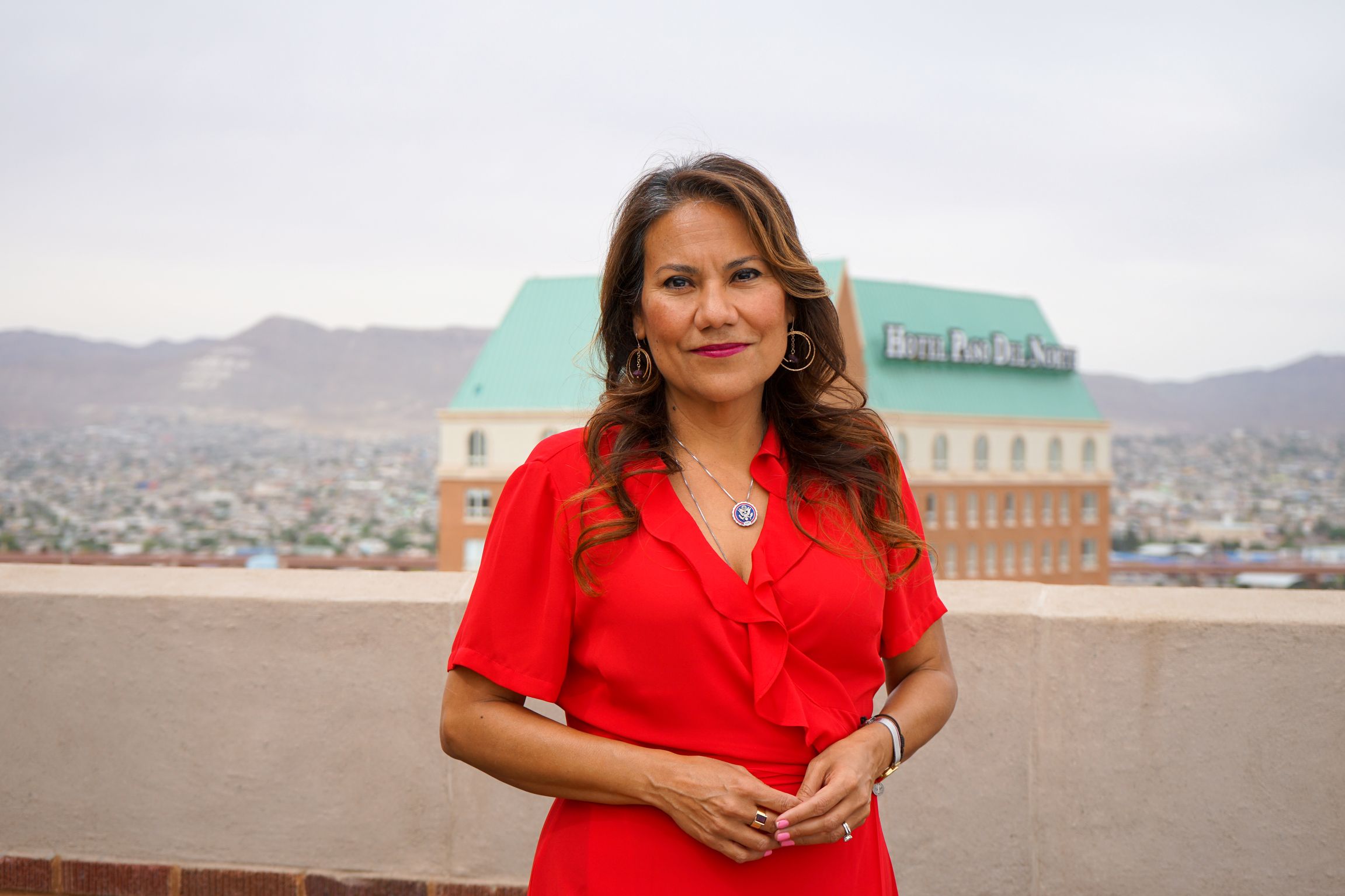 Veronica Escobar is pictured standing outdoors in a red dress with mountains in the background.