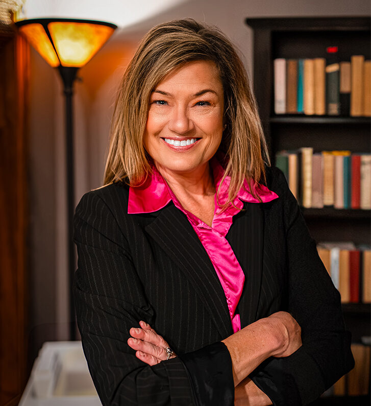 Sarah Corkey smiling in a black blazer and a hot pink shirt in a library.